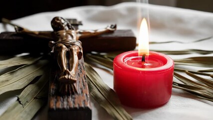 Jesus Christ crucifix with flickering red candle and dry palm frond for religious devotion and prayer.