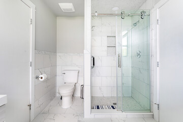 Modern white bathroom with glass shower and marble tile, clean minimalist interior design with bright natural light