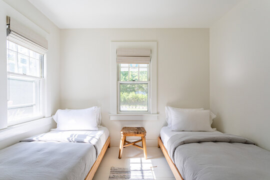 Bright minimalist twin bedroom with two single beds and natural light, neutral modern interior with simple furniture and clean design