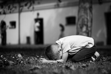 A child is kneeling on the grass with their head down, appearing upset or focused, in a black and white image.