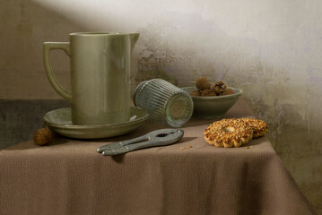 An autumn still life in calm tones. A jug on a table, dry branches, nuts, and grapes.