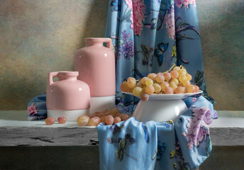 Still life with soft pink jugs, pink and blue satin fabric and pink grapes