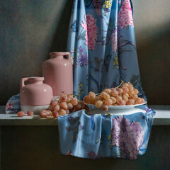 Still life with soft pink jugs, pink and blue satin fabric and pink grapes