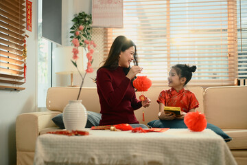 Mother and daughter sit together decorating red lanterns ornaments for Chinese New Year, sharing a joyful family moment