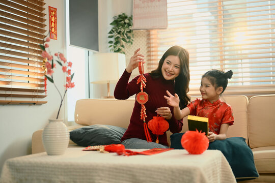 Mother and daughter sit together decorating red lanterns ornaments for Chinese New Year, sharing a joyful family moment