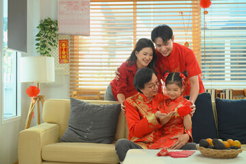 Multigenerational family gathers closely as grandparents and parents smile while a young girl holds a red gift during Chinese New Year.