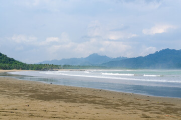 Cloudy atmosphere over Rajegwesi Beach in Banyuwangi features wide sandy shores, gentle waves, and forested hills, serving as a quiet coastal retreat and boat transit point to Green Bay. South Java.