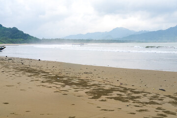 Cloudy atmosphere over Rajegwesi Beach in Banyuwangi features wide sandy shores, gentle waves, and forested hills, serving as a quiet coastal retreat and boat transit point to Green Bay. South Java.