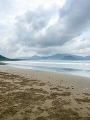 Cloudy atmosphere over Rajegwesi Beach in Banyuwangi features wide sandy shores, gentle waves, and forested hills, serving as a quiet coastal retreat and boat transit point to Green Bay. South Java.