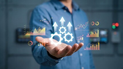 Businessman holding holographic interface showing upward trending business growth statistics, gears, and performance improvement charts in a modern industrial setting