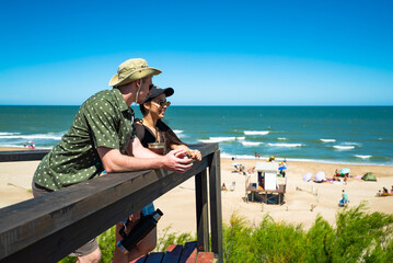 A man and a woman are sitting on a wooden platform overlooking the beach
