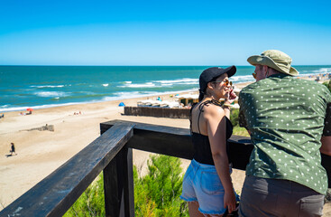 A man and a woman are sitting on a wooden platform overlooking the beach