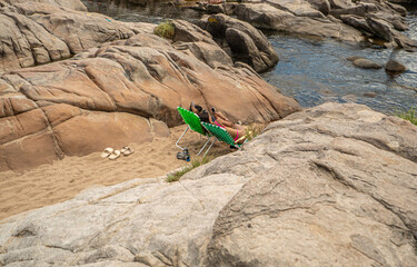 A person is laying on a green lawn chair on a beach