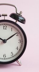 Retro black alarm clock against a clean light pink background, close up shot.