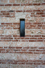 A small rectangular window in a red brick wall. A window seen on church or monastery buildings.