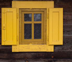 Wooden window with yellow shutters. Yellow wooden window with wooden acorns. The window is divided into four parts by wooden moldings. Old building.