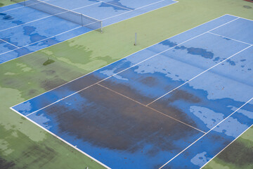 Blue tennis courts photographed from above. The pitches are dirty because of the rain that fell the previous days.
