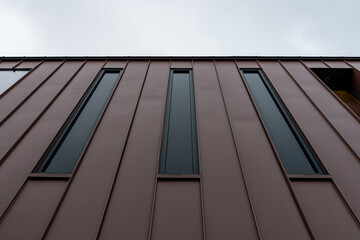 Obraz premium Vue en contre-plongée d’une façade contemporaine en bardage métallique brun avec ouverture architecturale, illustrant un design moderne et minimaliste.