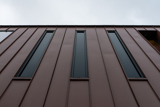 Vue en contre-plong&eacute;e d&rsquo;une fa&ccedil;ade contemporaine en bardage m&eacute;tallique brun avec ouverture architecturale, illustrant un design moderne et minimaliste.