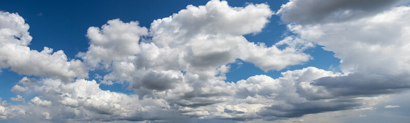 Panoramic view of a bright blue sky with voluminous white and grey cumulus clouds on a sunny day creating a sense of space and freedom