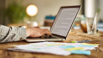 Focused individual using laptop to draft a clear detailed grant proposal with notes and reference materials spread on a wooden desk.