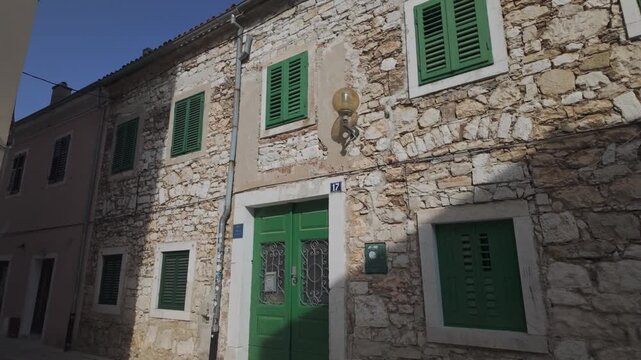 Charming facade of a historic residential apartment made of time-worn stones. Romantic looking-up street scenery in Porec, Croatia. Mediterranean house exterior with green door and window shutters.