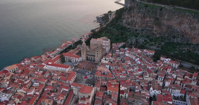 Aerial view of Cefalu Cathedral, a majestic structure amid the terracotta rooftops cascading towards the azure sea, Cefalu, Sicily, Italy.