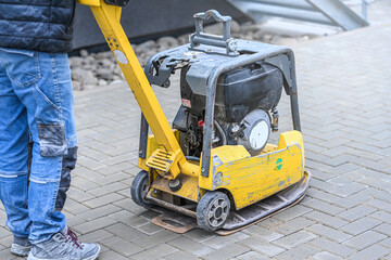 Fototapeta premium Working with vibro-compaction plate to compact self-locking blocks in their laying bed. Vibrating plate in construction.