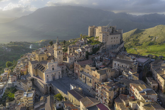 Aerial view of the ancient Caccamo Castle perches atop a hill, its stone walls glowing warmly in the soft light, overlooking the town below, Caccamo, Sicily, Italy.