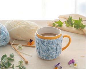 Warm Coffee Mug with Knitted Cozy and Yarn on Wooden Table 