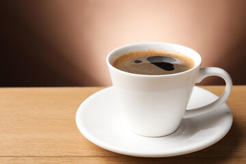 Aromatic coffee in cup on wooden table, closeup. Space for text
