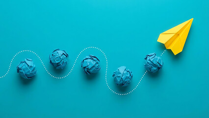Yellow paper airplane soaring above crumpled blue paper balls on a turquoise background, symbolizing innovation and overcoming obstacles