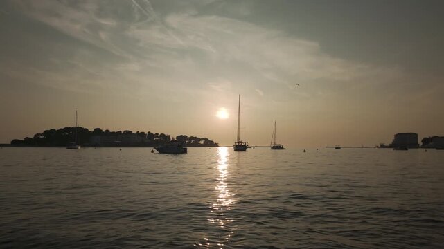 Dreamy Adriatic Sea sunset scenery with seagulls flying above gently rocking boats. Port of Porec, Croatia with calm water surface, tranquil ripples, and beautiful reflections in golden evening lights