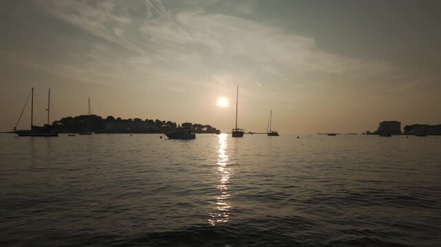 Sunset above the Adriatic Sea. View from the port of Porec, Croatia in golden evening lights. Dreamy scenery of gently rocking boats with calm water surface, tranquil ripples and beautiful reflections
