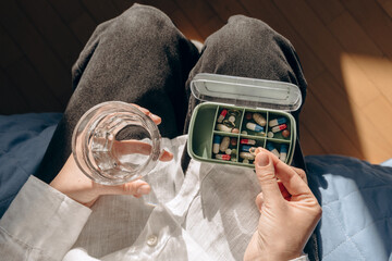 Close-up of hands placing pills into a green, compartmentalized pill organizer. Focus on daily medication, home health care, and personal wellness management.