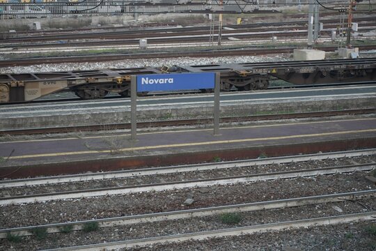 View of the railway tracks in Novara, Italy, featuring a warning sign along the tracks, highlighting the urban train infrastructure and safety elements of the station environment.