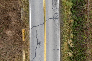 Aerial View Of A Cracked Road With Center Double Yellow Lines And Surrounded By Vegetation In BC,...