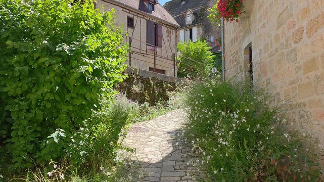 Pretty cobble stone street in the village of Autoire, France with flowers. Handheld walking motion.