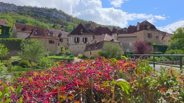 Beautiful view of the village of Autoire, France with colorful red shrubs. Handheld upward panning motion.