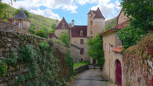 Beautiful street in the village of Autoire, France with medieval turreted architecture. Handheld downward panning motion.