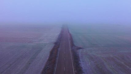 Drone Flying Slowly Above Rural Road Through Farmland in Foggy Winter Morning