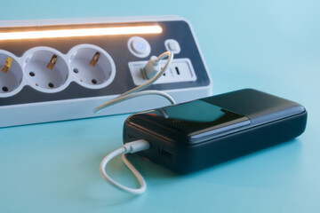External battery pack connected to a multi socket block with built-in charger. Concept of modern electrical equipment and tech gadgets on a turquoise background. Photo