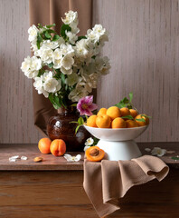 Still life with a plate of apricots, a bouquet of jasmine in a vase in yellow, orange and brown tones