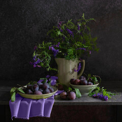 Still life with a plate of plums, a jug with a bouquet of wild flowers in blue-lilac and gray-black tones