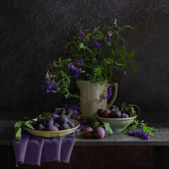 Still life with a plate of plums, a jug with a bouquet of wild flowers in blue-lilac and gray-black tones
