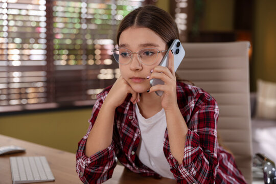 Teenage girl talking on smartphone at table indoors, space for text - Powered by Adobe