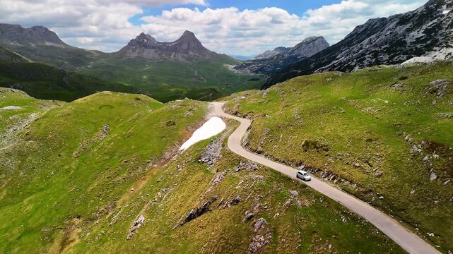 Aerial drone view of the mountains in Durmitor National Park, Montenegro. A car drives along a scenic mountain road through the forest and towering mountains. Beautiful mountain landscape.