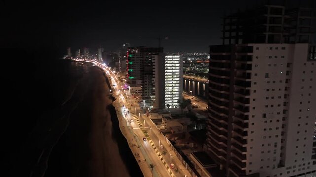 Im&aacute;genes a&eacute;reas nocturnas del Malec&oacute;n de Mazatl&aacute;n con calles y edificios iluminados a lo largo de la costa.
