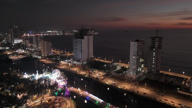 Im&aacute;genes a&eacute;reas nocturnas del Malec&oacute;n de Mazatl&aacute;n con calles y edificios iluminados a lo largo de la costa.
