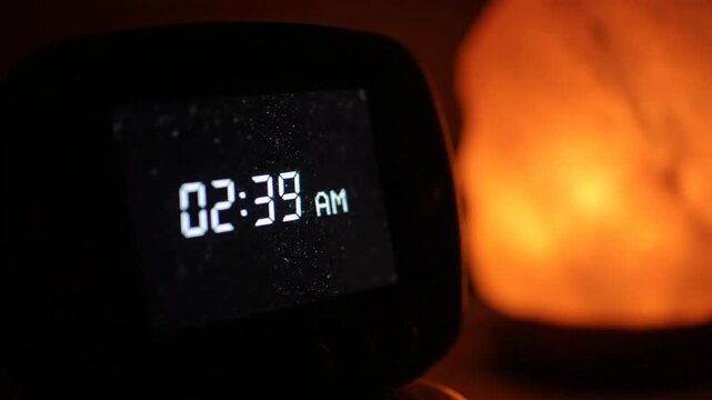 Digital alarm clock displaying 2:37 AM with warm glow salt lamp in the night. Time, late, sleep, dark, wake, bedside concept.